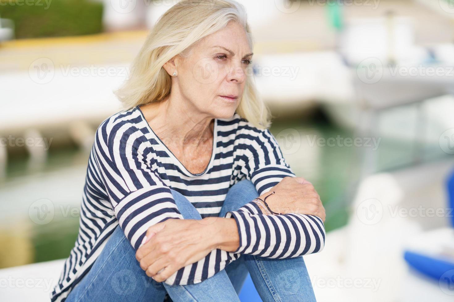 anciana mirando serenamente al horizonte, sentada en un puerto marítimo. foto