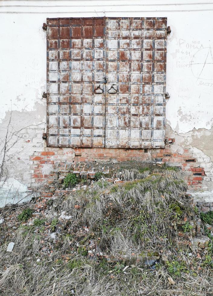 Ancient doors of the monastery with a ruined staircase.The ramshackle walls were overgrown with grass.Metal-bound door. photo