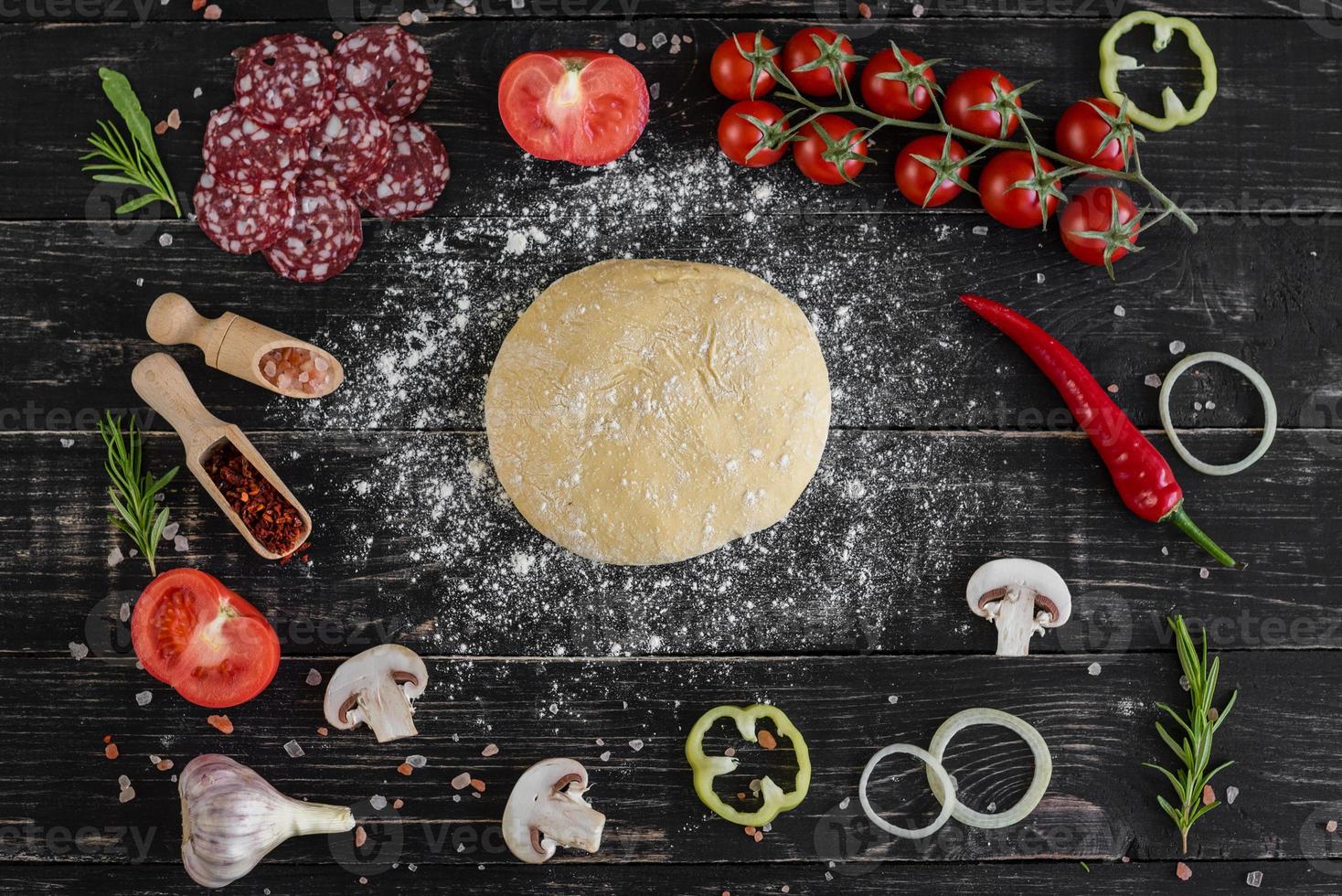 Raw dough for pizza with ingredients and spices on black background photo