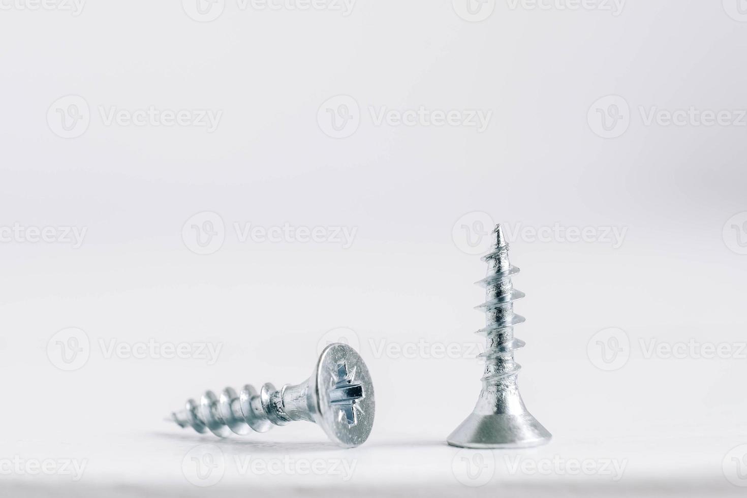 Two metal screws for wood on white wooden background photo