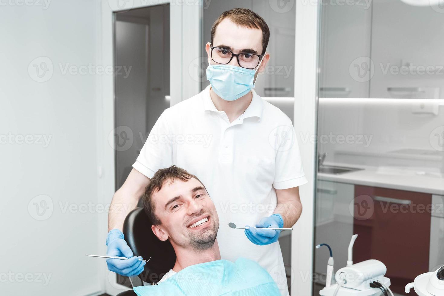 el dentista examina los dientes de un paciente masculino en la silla de un dentista foto