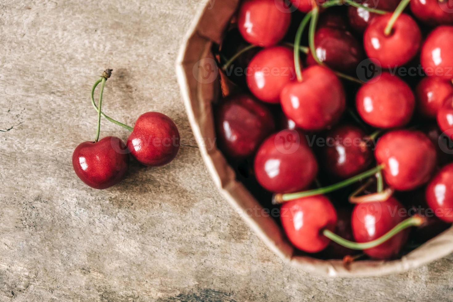 Fresh ripe cherries in a paper bag on wooden background. Top view. Copy, empty space for text photo