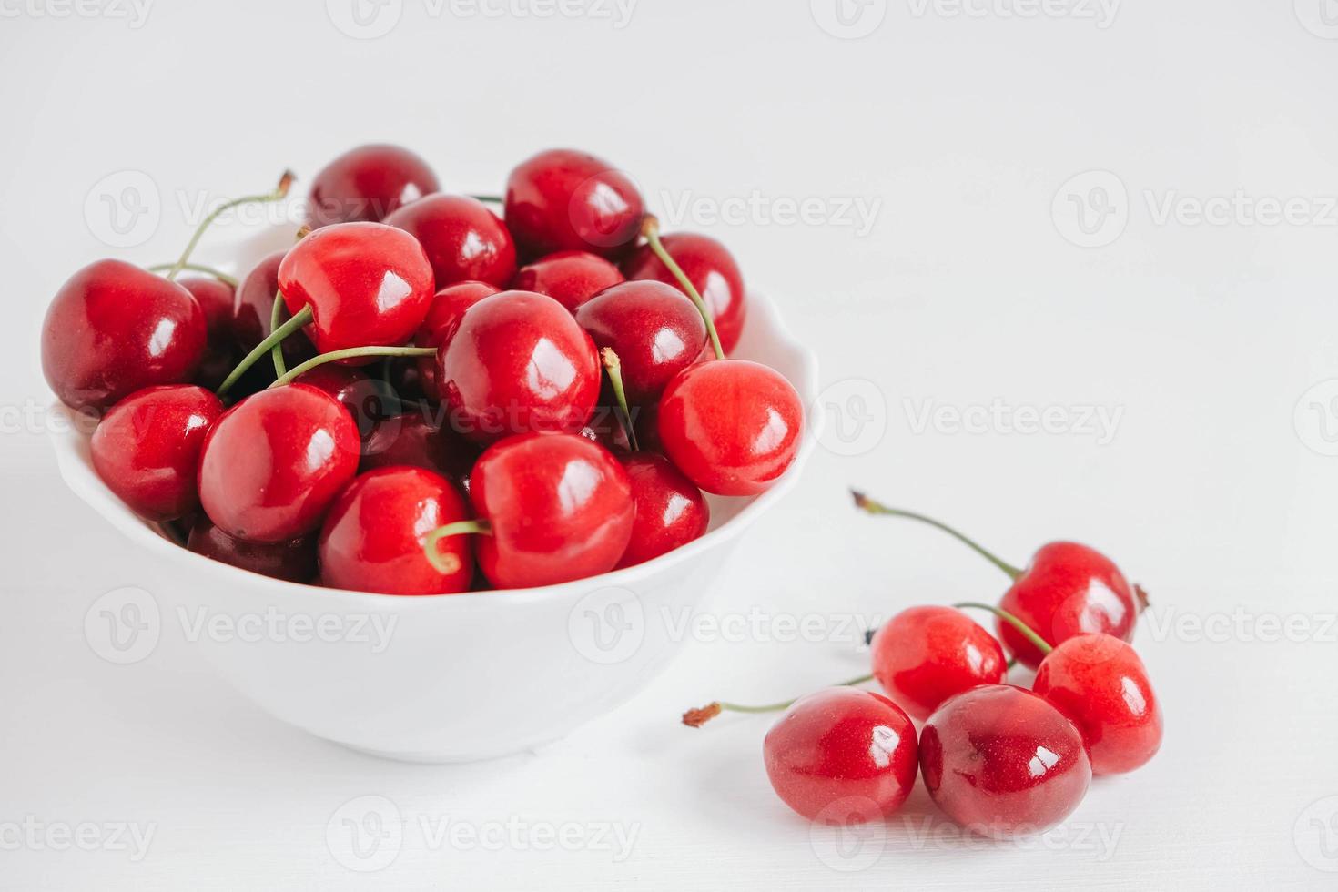 cerezas rojas frescas y jugosas en un plato blanco sobre fondo blanco de madera foto