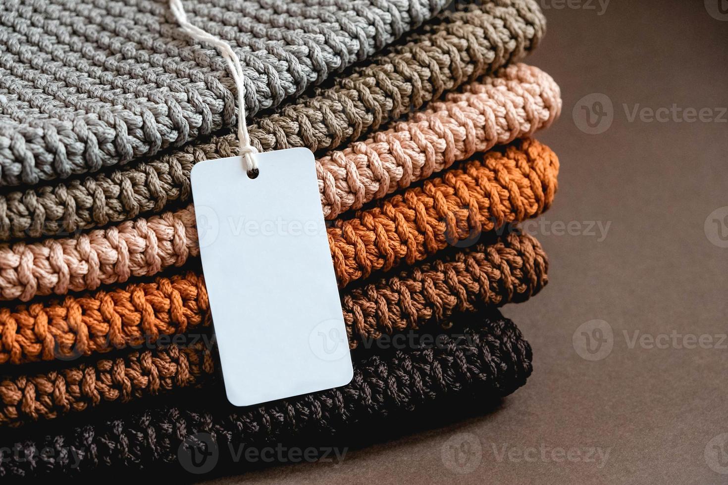 Stack of knitted material from threads of brown, orange, gray colors with an empty price tag on a brown background photo