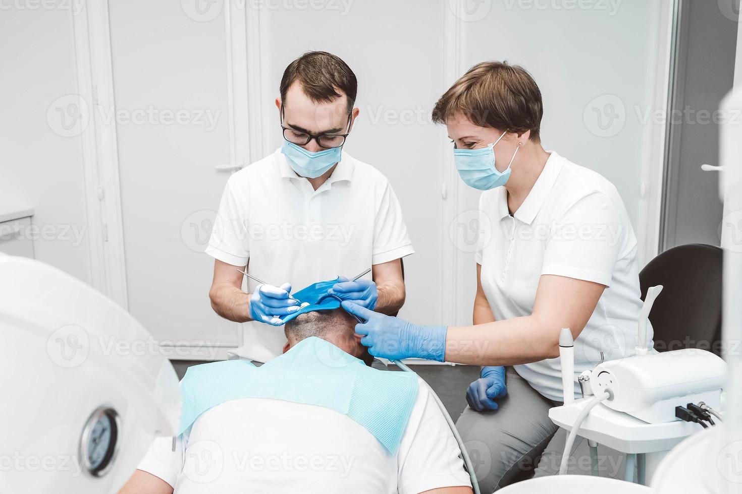 el dentista y su asistente tratan a un paciente masculino en una clínica dental. dentistas con máscaras médicas trabajando con los dientes del cliente foto