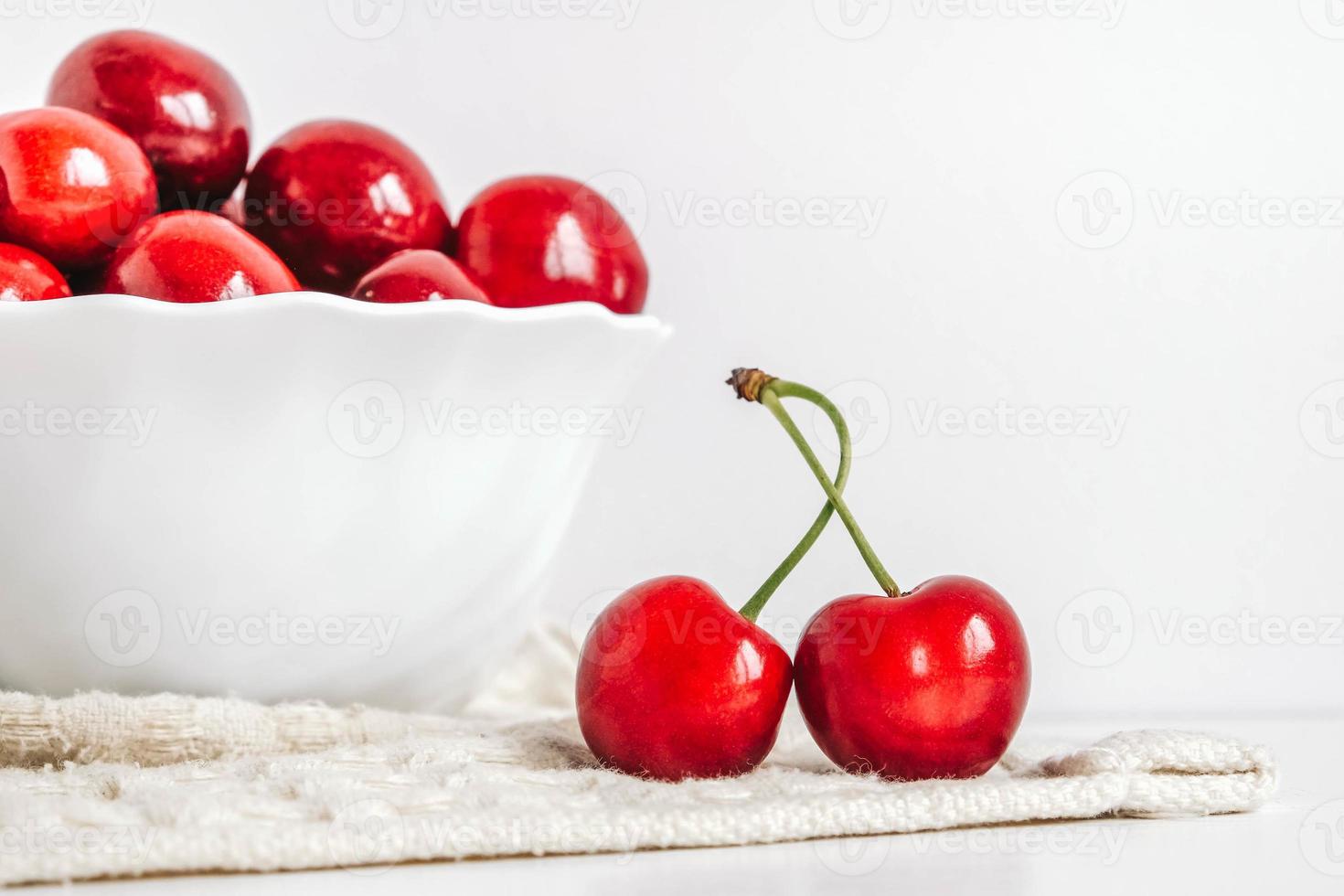 cerezas rojas frescas y jugosas en un plato blanco sobre el fondo blanco de madera. copiar, espacio vacío para texto foto