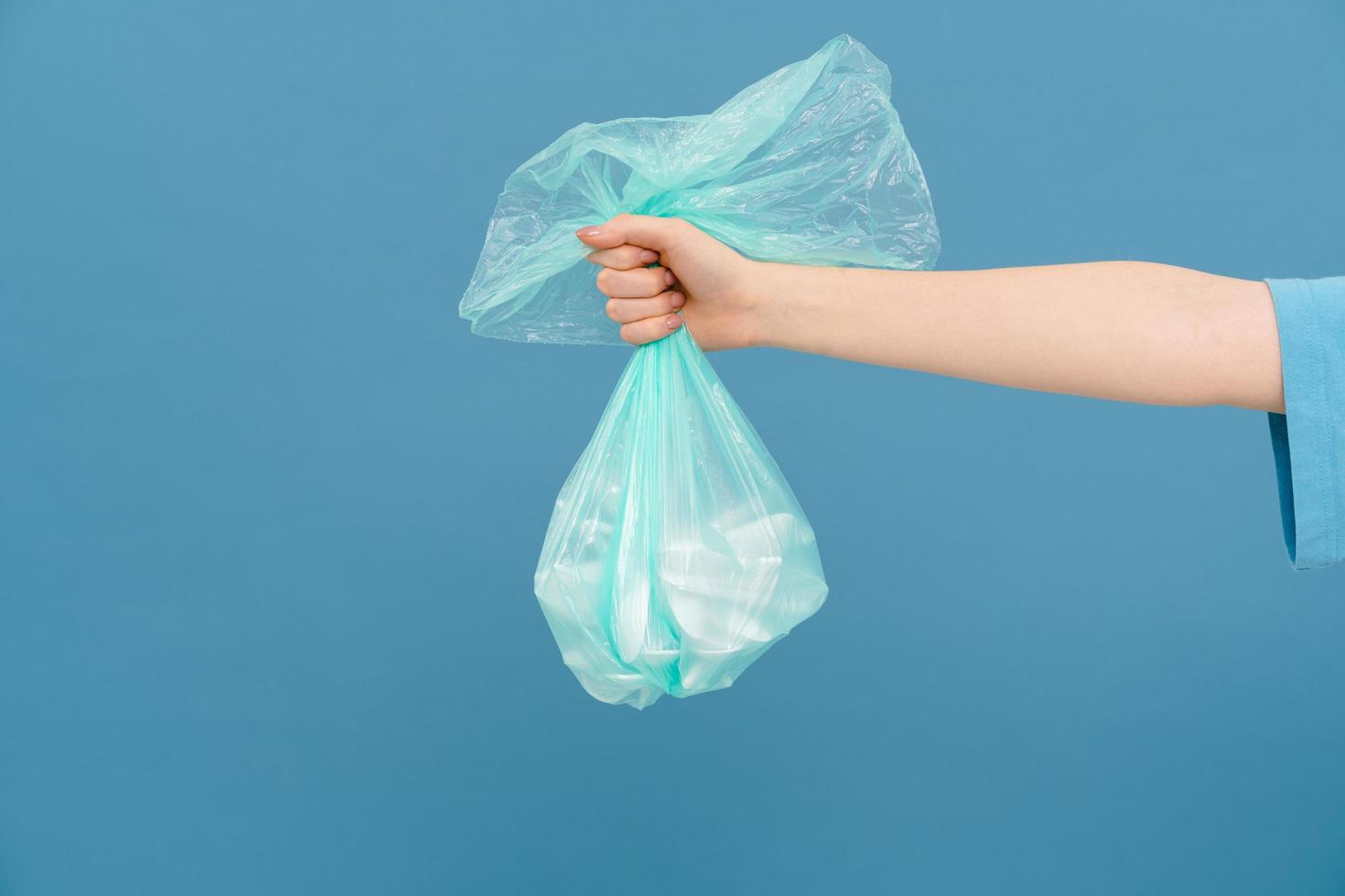 Young woman wearing t-shirt holding plastic trash bag with one arm photo