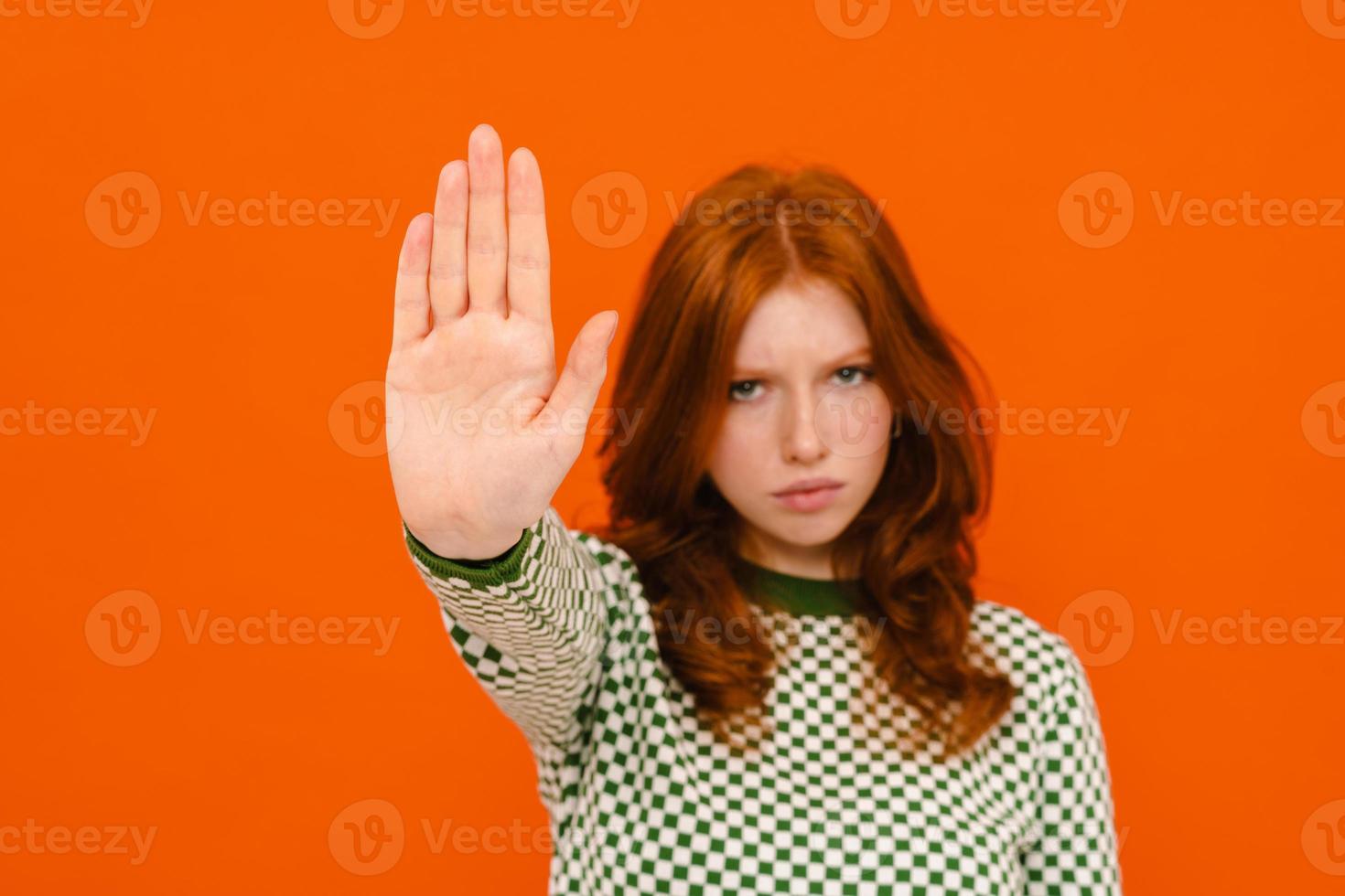 Displeased ginger-haired woman in plaid sweater showing stop gesture photo