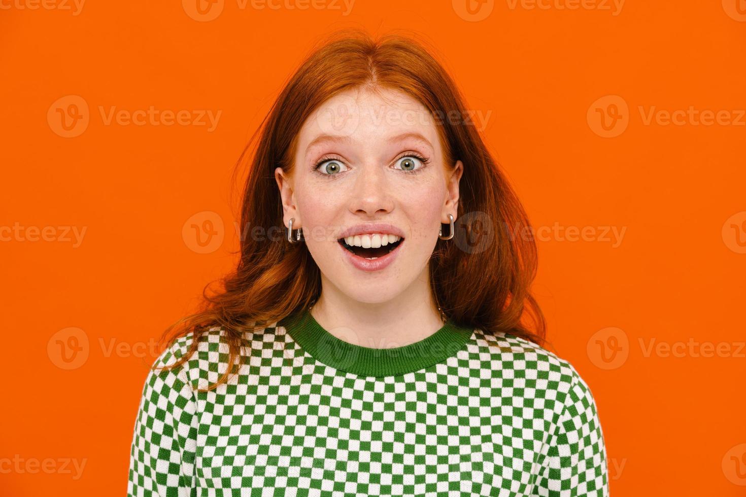 Excited ginger-haired woman in plaid sweater expressing surprised look on her face to camera photo