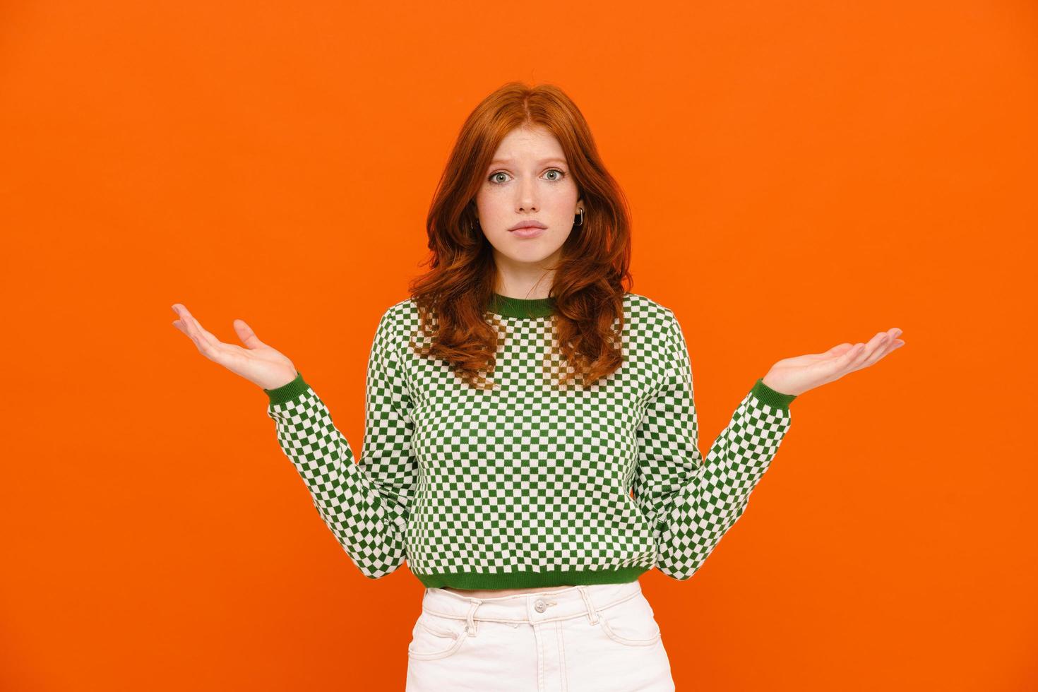 Confused woman with ginger hair in plaid sweater holding copyspace photo