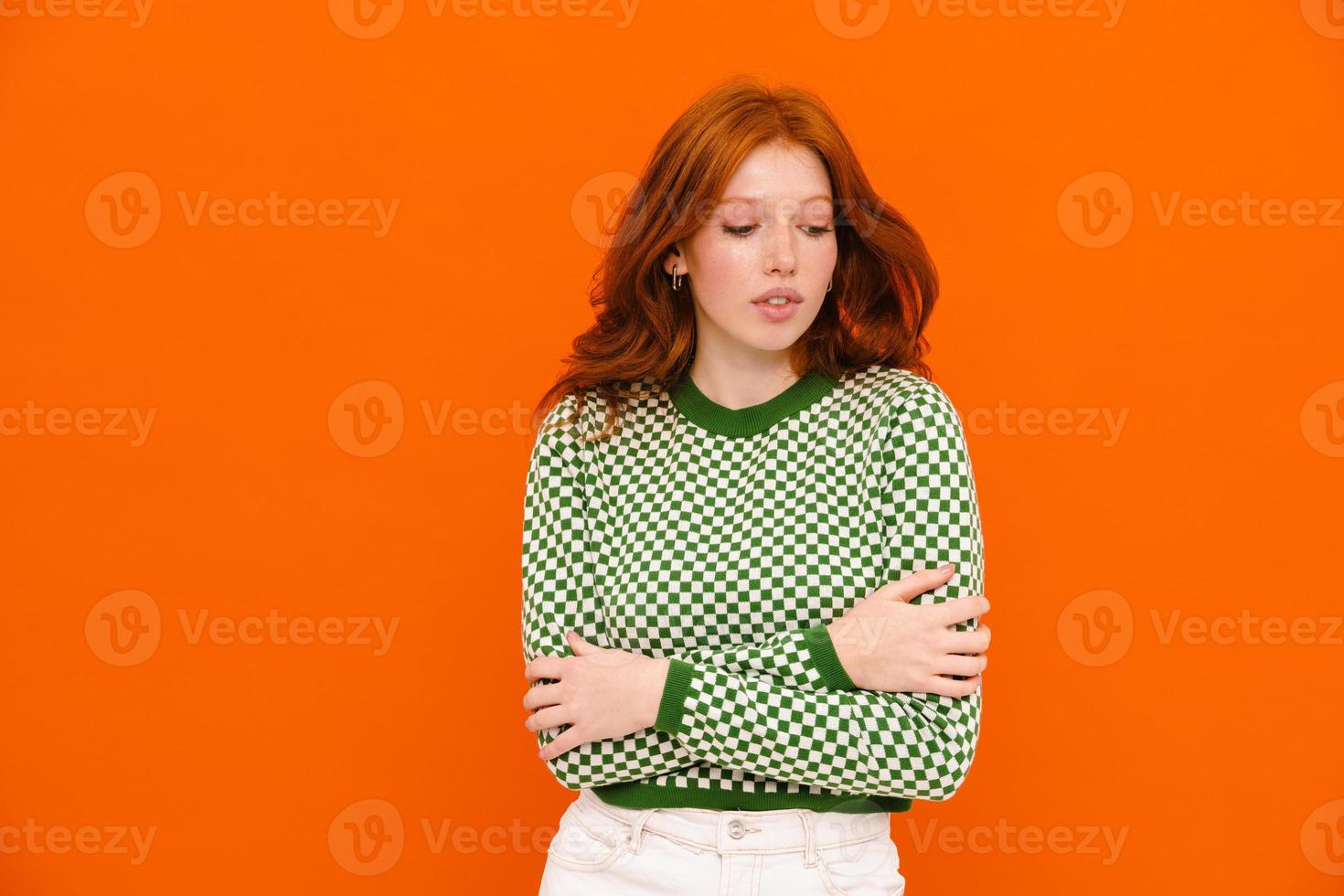 Young ginger-haired woman in plaid sweater looking downward photo