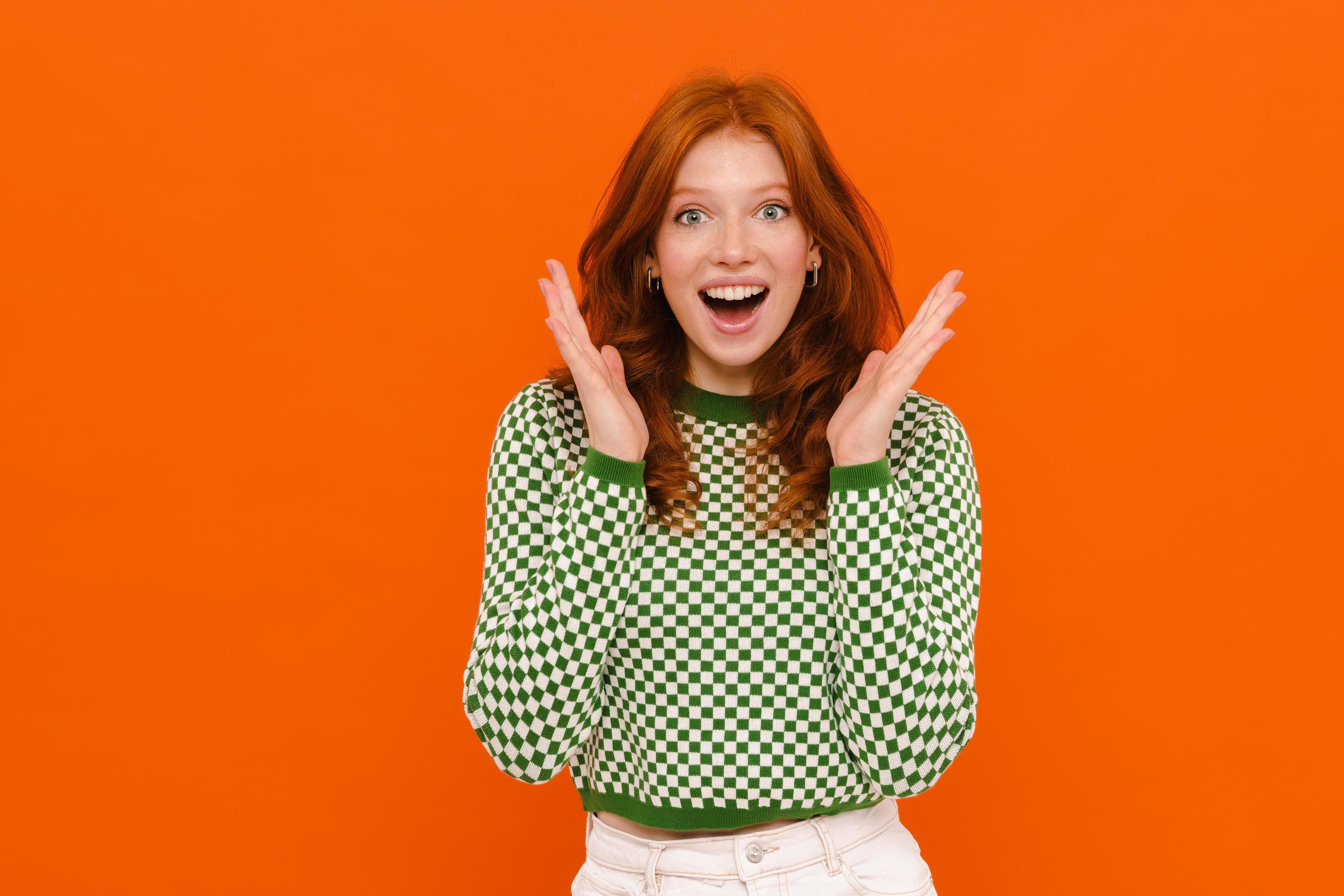 Excited ginger-haired woman in plaid sweater expressing surprise at camera photo