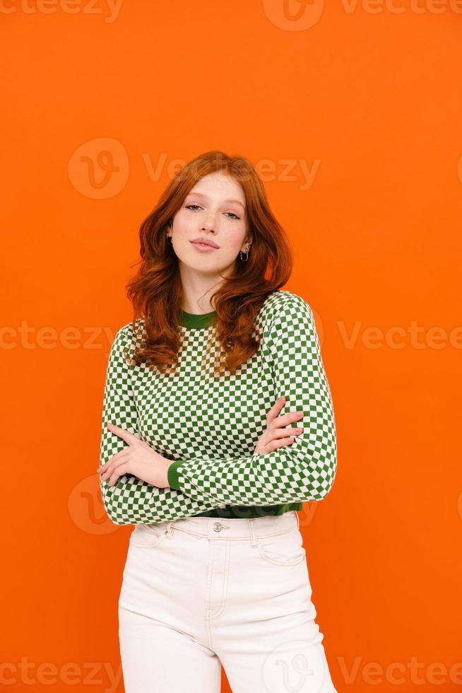 Young woman with ginger hair in plaid sweater posing with arms crossed photo