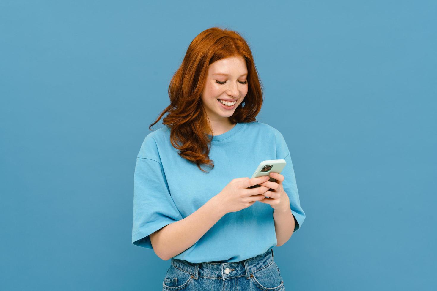 joven pelirroja con camiseta sonriendo y usando celular foto