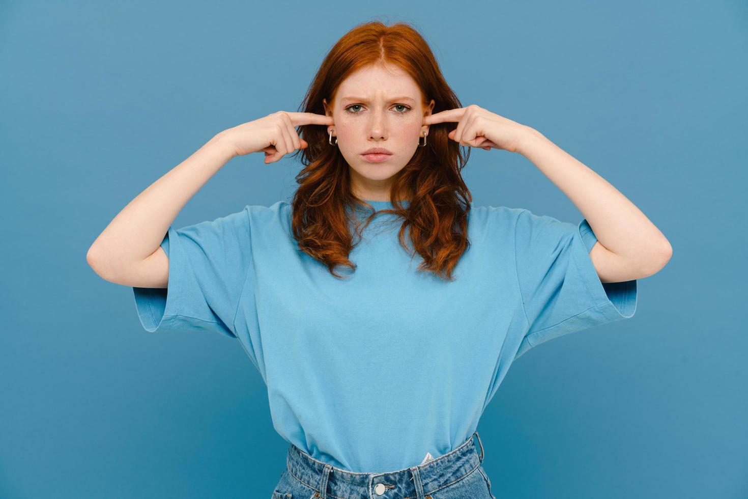 Young woman with ginger hair wearing t-shirt plugging her ears photo