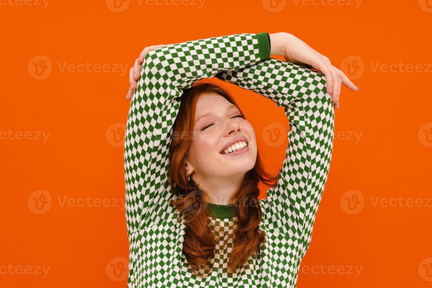 Young ginger-haired woman in plaid sweater smiling at the camera photo