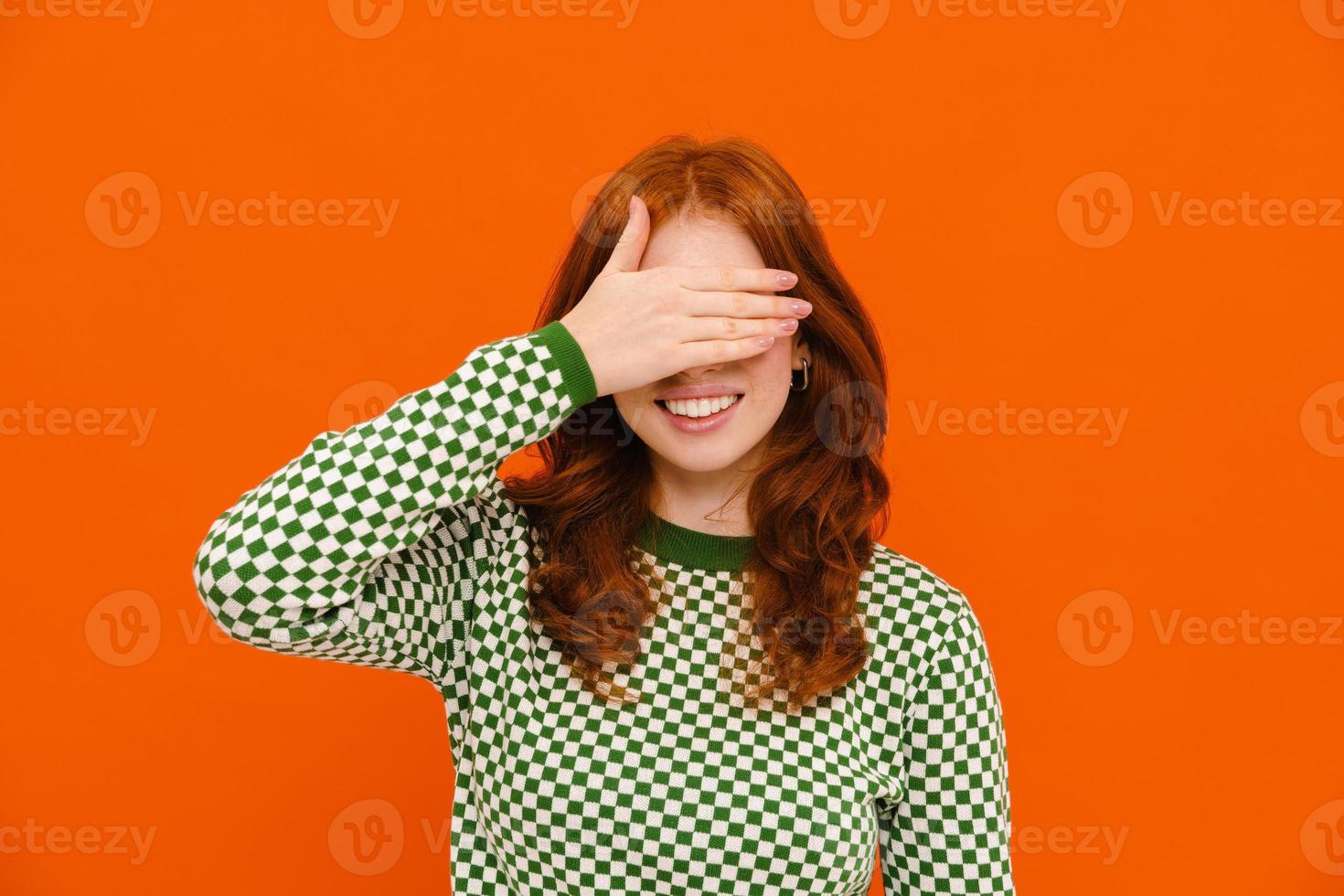 Young ginger woman in plaid sweater smiling and blocking her face photo