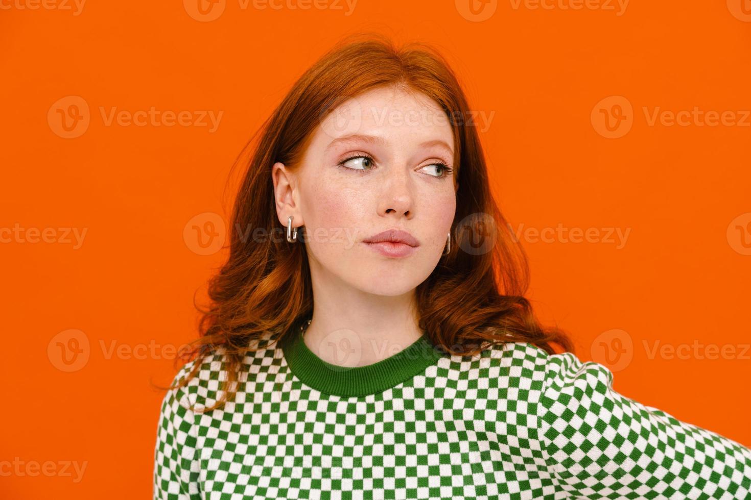 Puzzled ginger-haired woman in plaid sweater looking aside photo