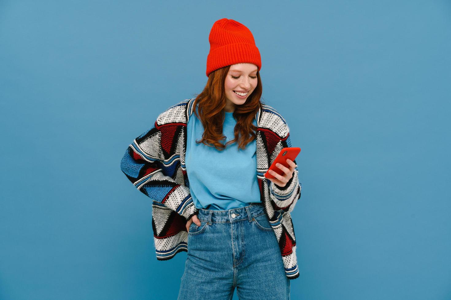 mujer pelirroja sonriente con suéter multicolor usando un celular foto