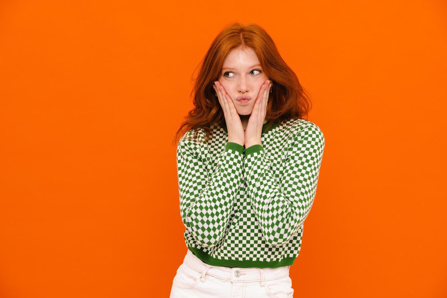 Displeased ginger-haired woman in plaid sweater grimacing at camera photo