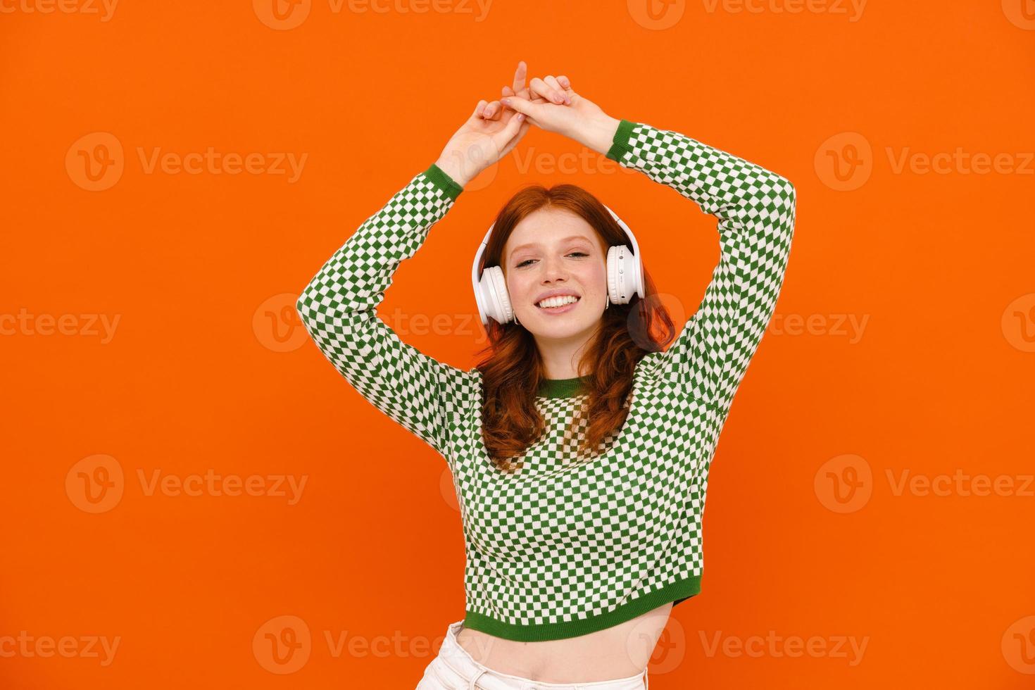 Happy ginger-haired woman in plaid sweater dancing with headphones photo