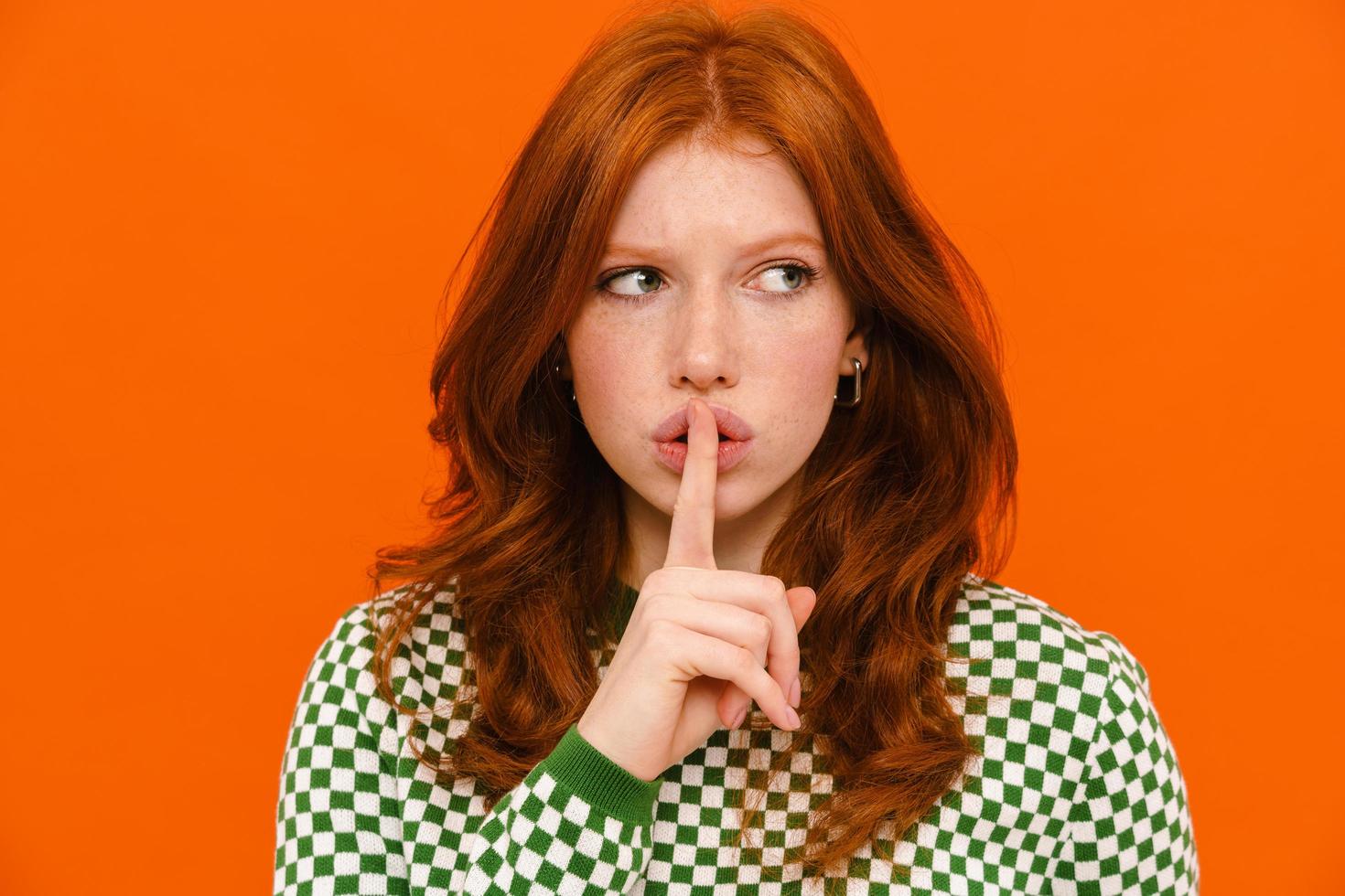 Displeased ginger-haired woman in plaid sweater showing silent gesture photo