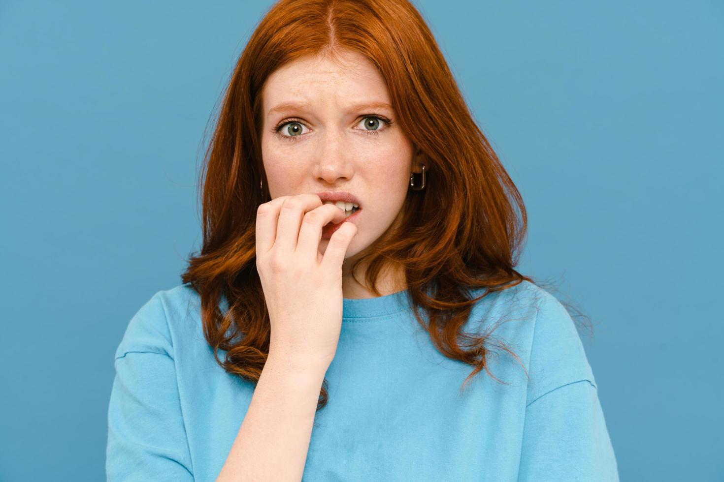 Scared woman with ginger-colored hair wearing t-shirt biting her fingers photo