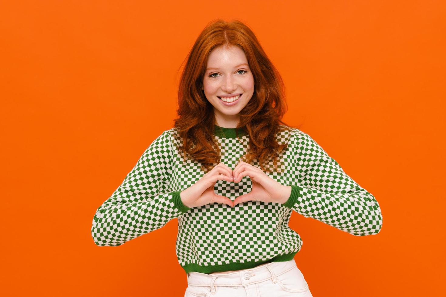 Ginger woman in plaid sweater smiling and showing heart gesture photo