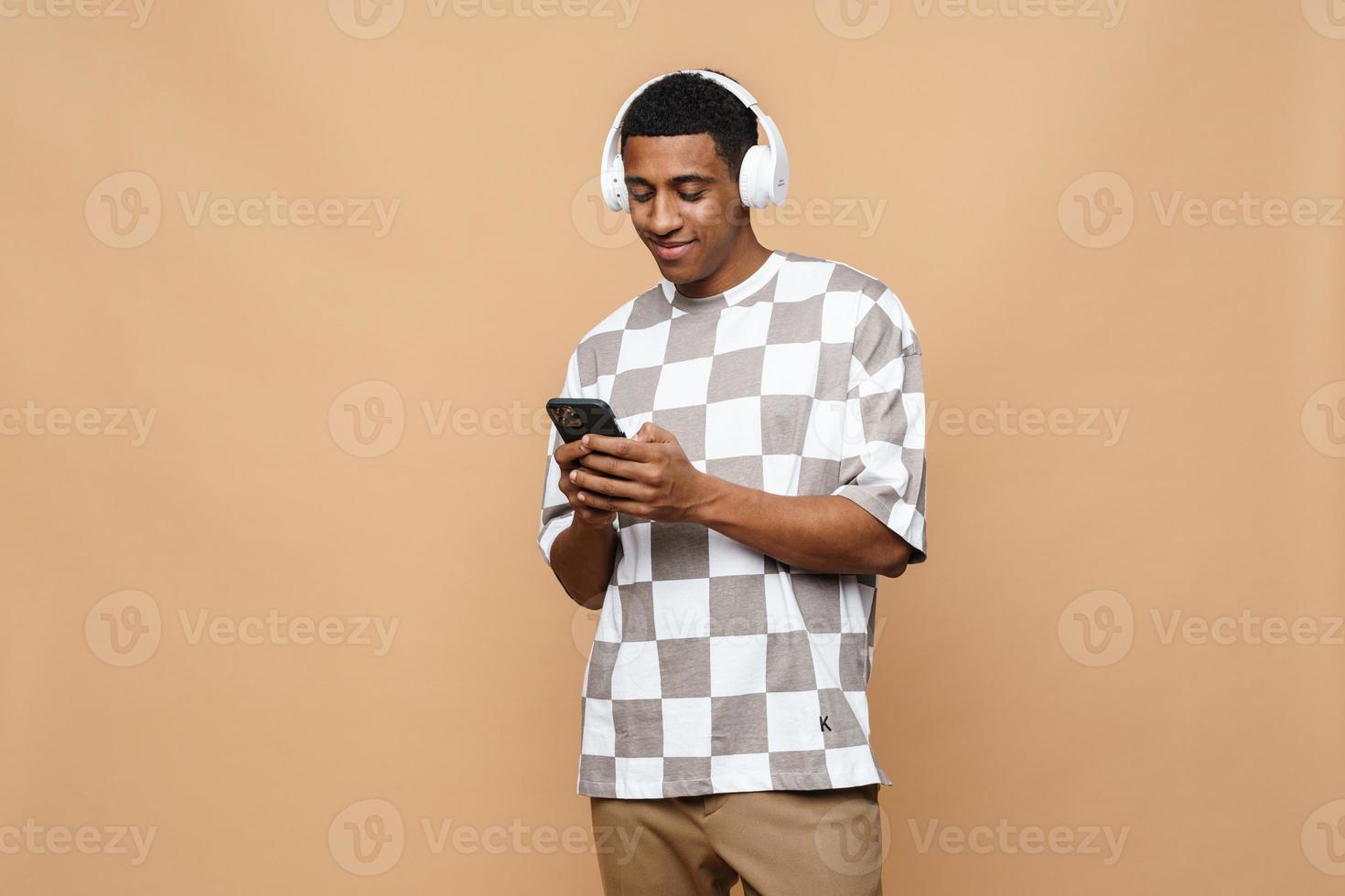 hombre africano alegre enviando mensajes de texto por teléfono con auriculares foto