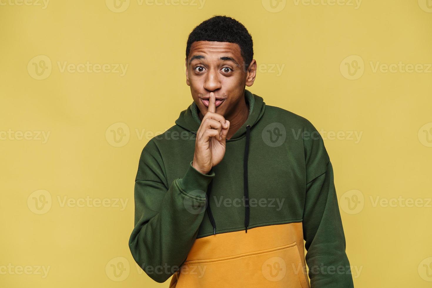 Positive African man in hoodie showing silence gesture photo