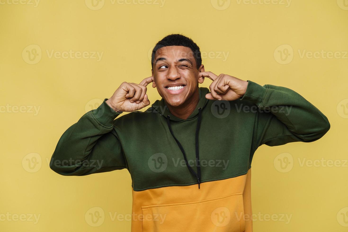 Happy African man in hoodie plugging ears photo