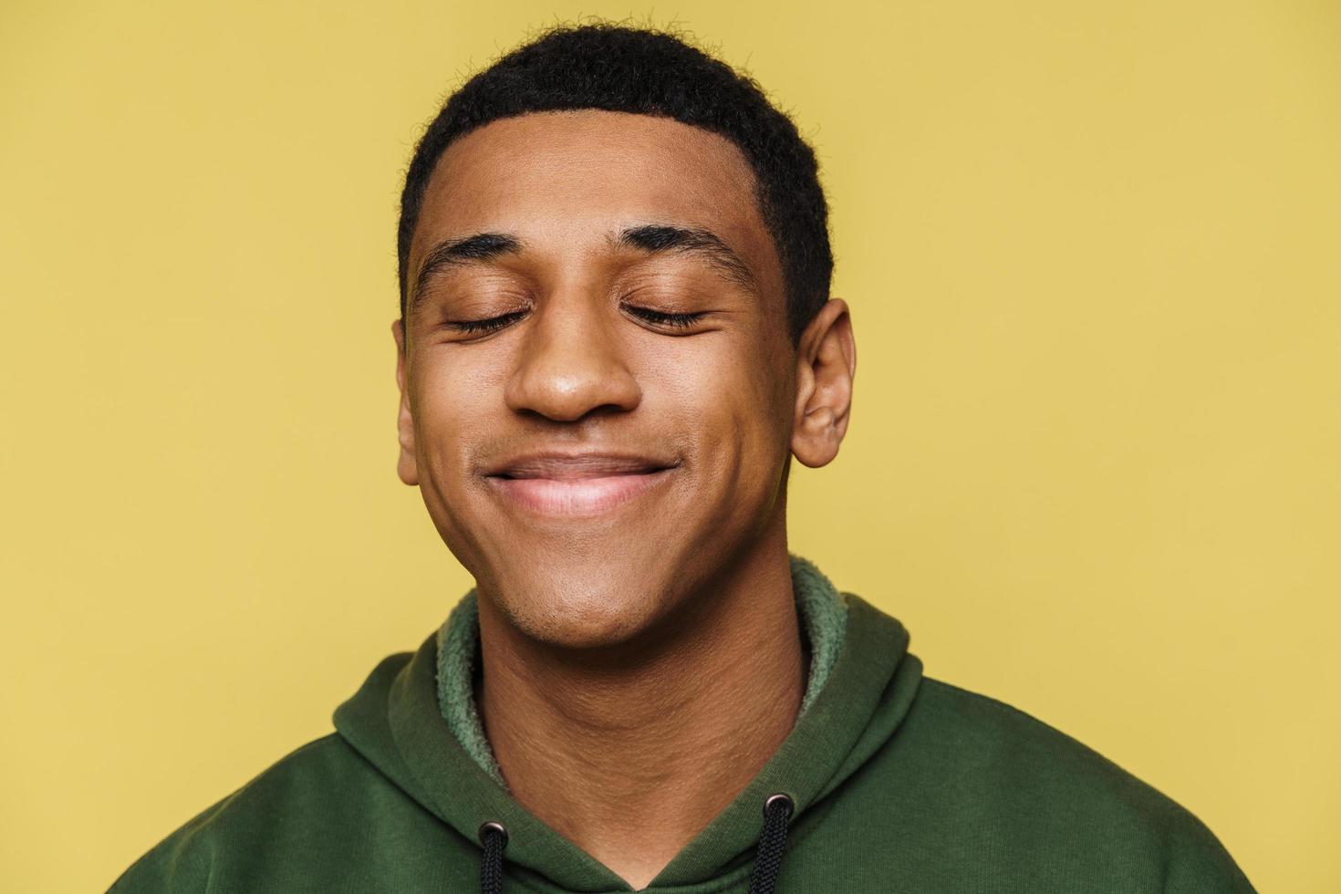 retrato de un hombre africano tranquilo y positivo con capucha parado con los ojos cerrados foto