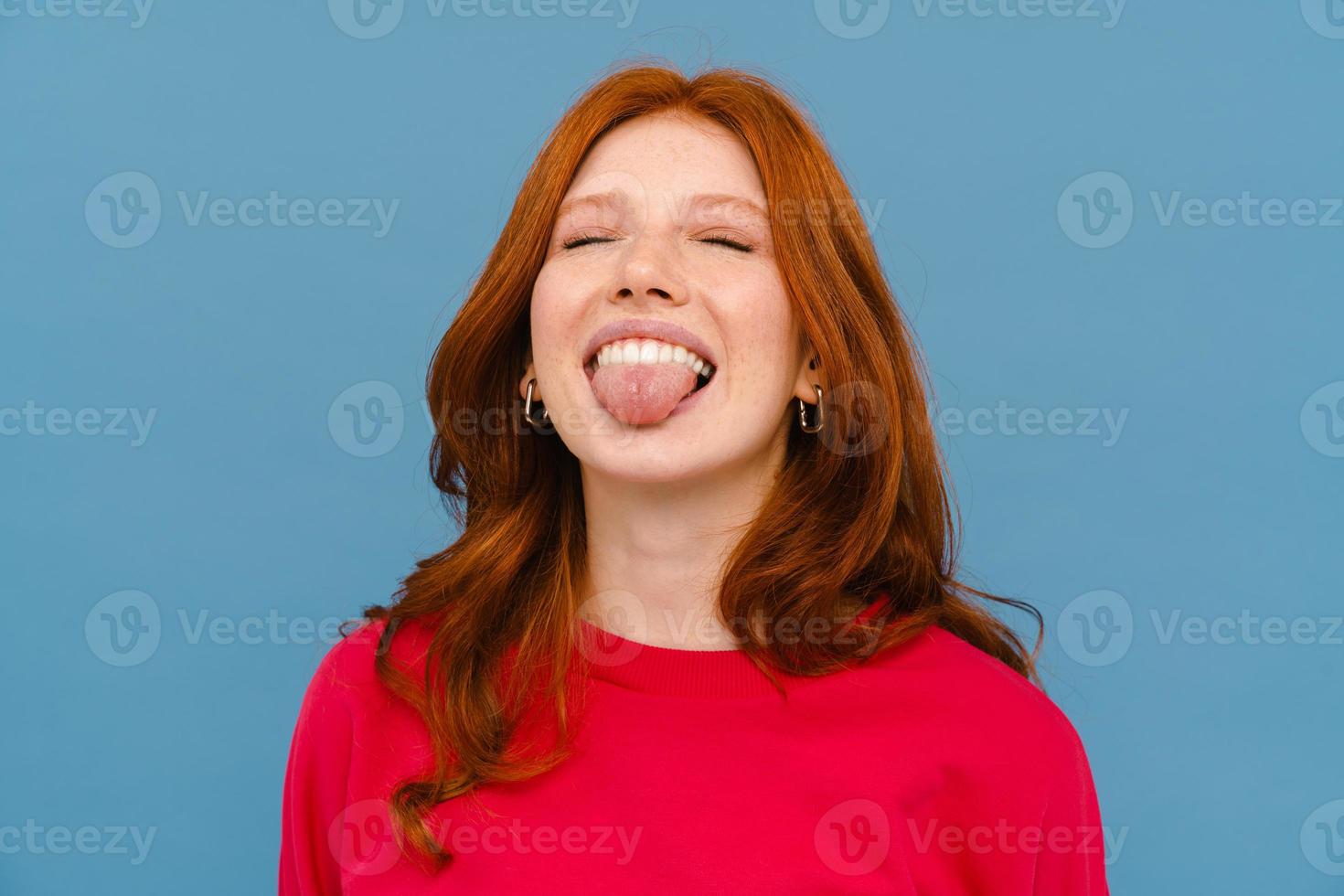 Ginger-haired woman wearing red sweater laughing while showing her tongue photo