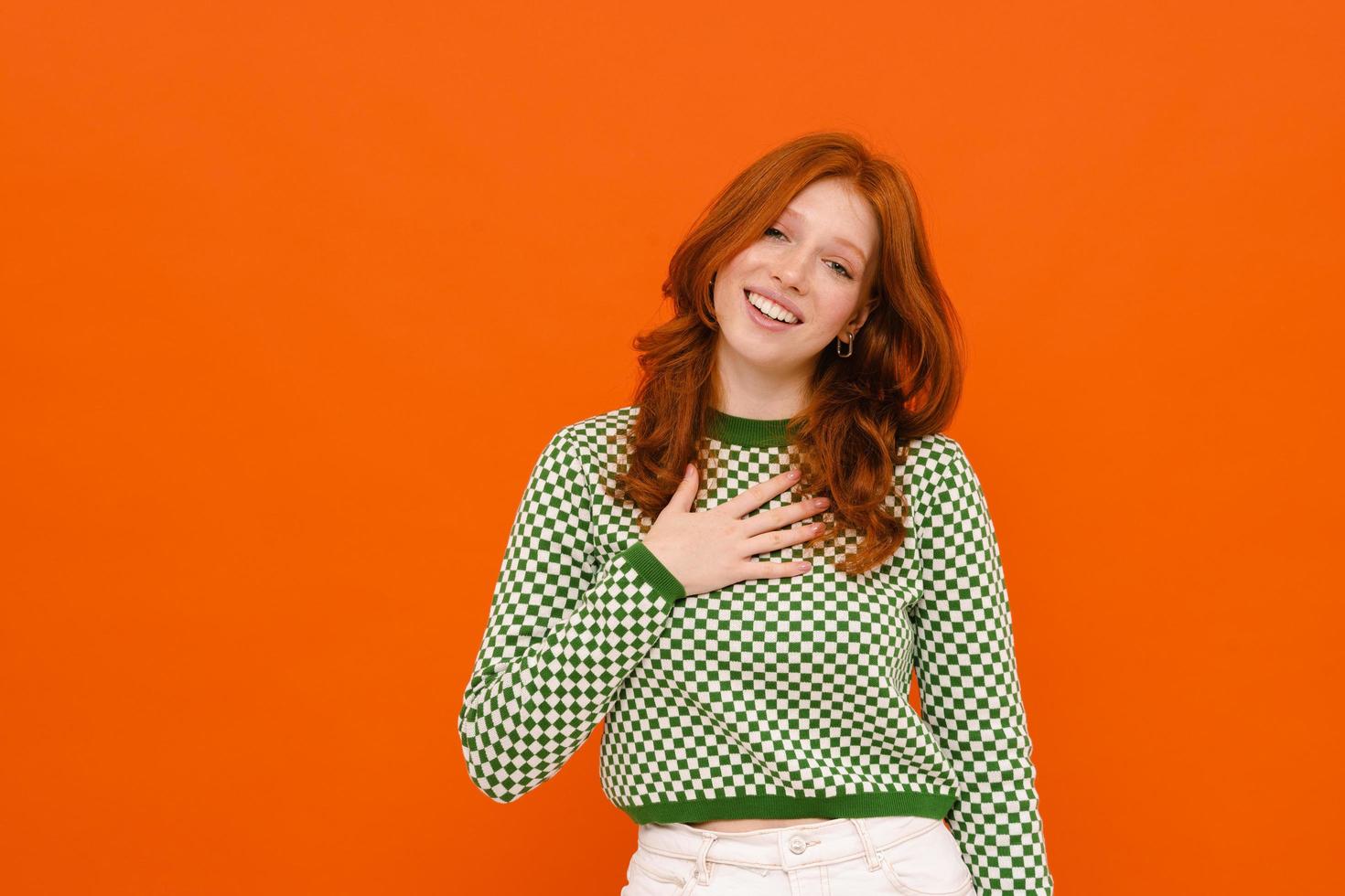 Ginger-haired woman in plaid sweater smiling and holding hand on her chest photo