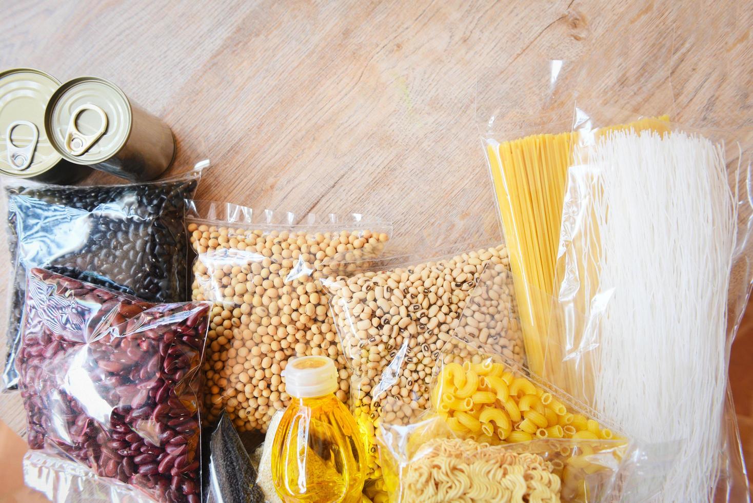 donaciones de comida con comida enlatada en el fondo de la mesa de madera pasta enlatada y comida seca no perecedera con frijoles guisantes aceite de cocina fideos instantáneos macarrones concepto de donación foto