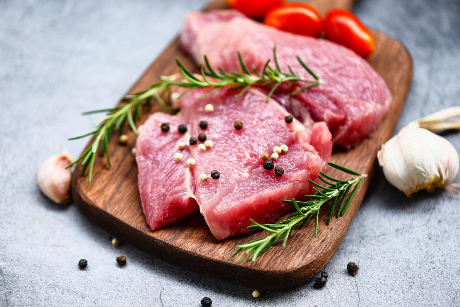Raw pork meat on wooden cutting board at kitchen table for cooking pork steak roasted or grilled with ingredients herb and spices - Fresh pork photo