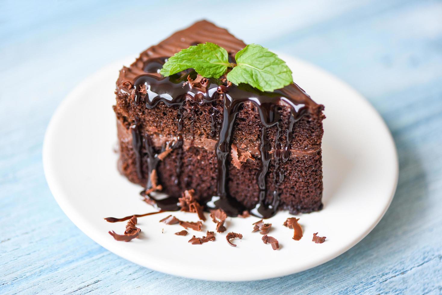 pastel de salsa de chocolate delicioso postre servido en la mesa - rebanada de pastel en un plato blanco con cobertura de chocolate y hoja de menta foto