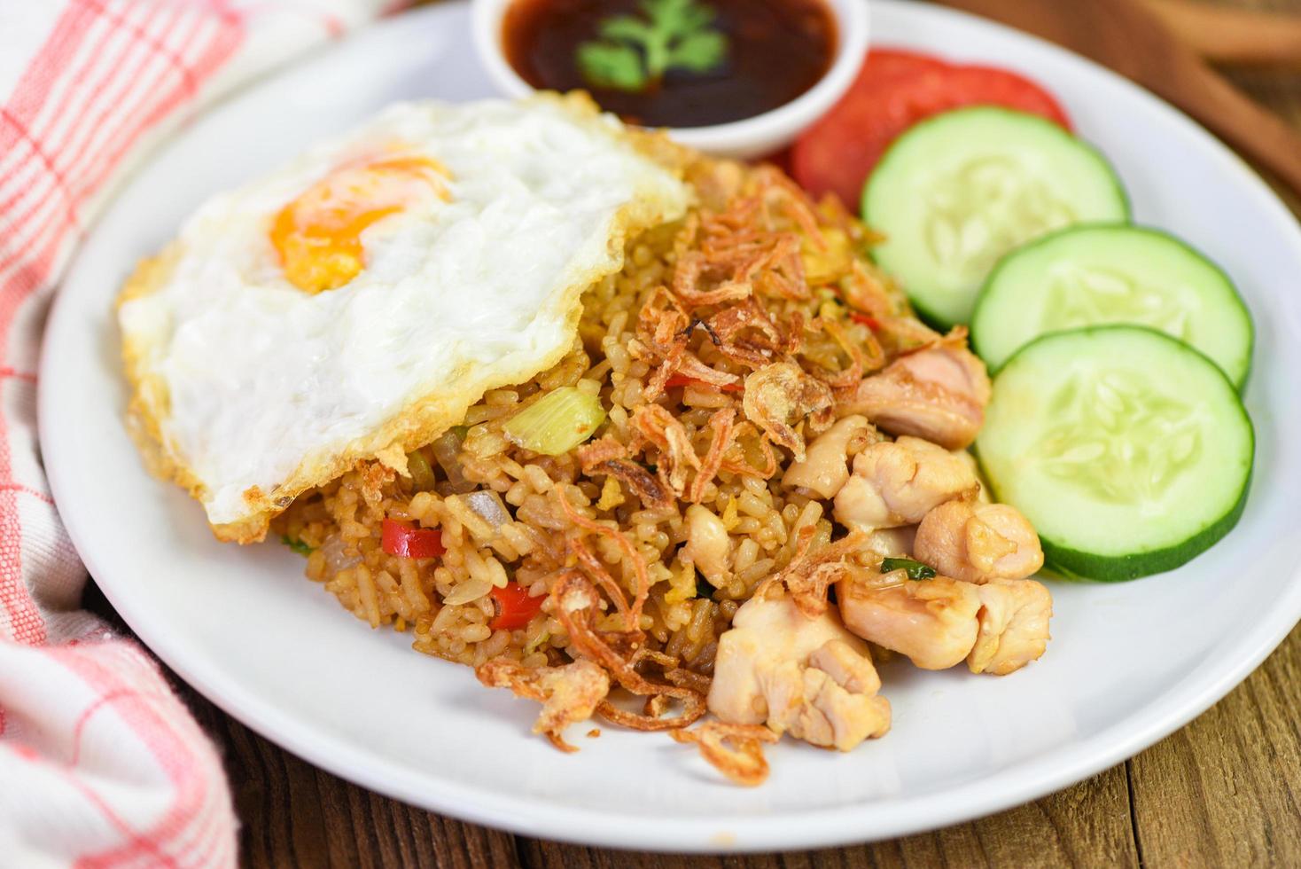 Nasi goreng fried rice chicken with egg tomato cucumber on white plate and sauce - Nasi Goreng Ayam indonesian food Asian photo