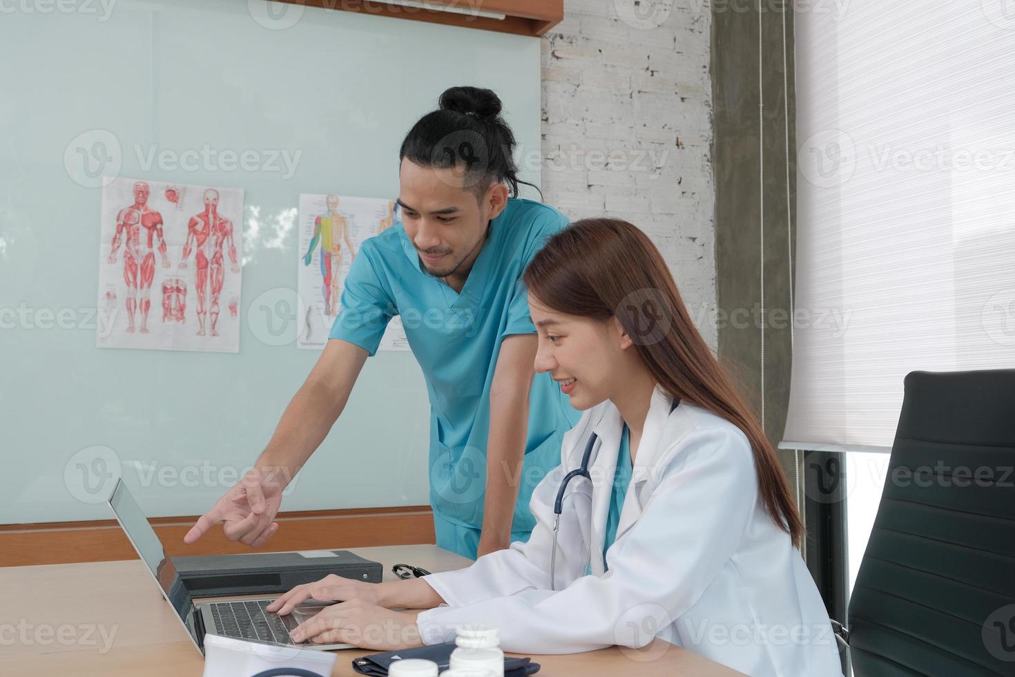 Healthcare team partners. Two uniformed young Asian ethnicity doctors are co-workers discussing medication in hospital's clinic office. Specialist persons are experts and professionals. photo