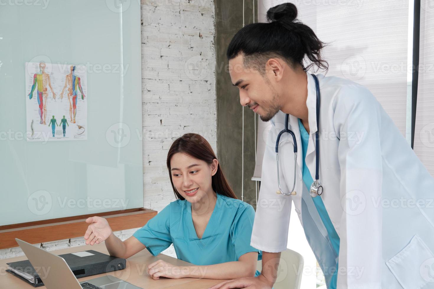 Healthcare team partners. Two uniformed young Asian ethnicity doctors are co-workers discussing medication in hospital's clinic office. Specialist persons are experts and professionals. photo