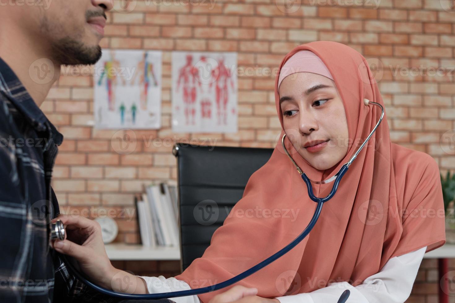 médico joven y bella mujer está examinando la salud del paciente masculino en la oficina de la clínica del hospital y asesorando con una sonrisa sobre los medicamentos. este especialista médico asiático es una persona islámica que lleva un hiyab. foto