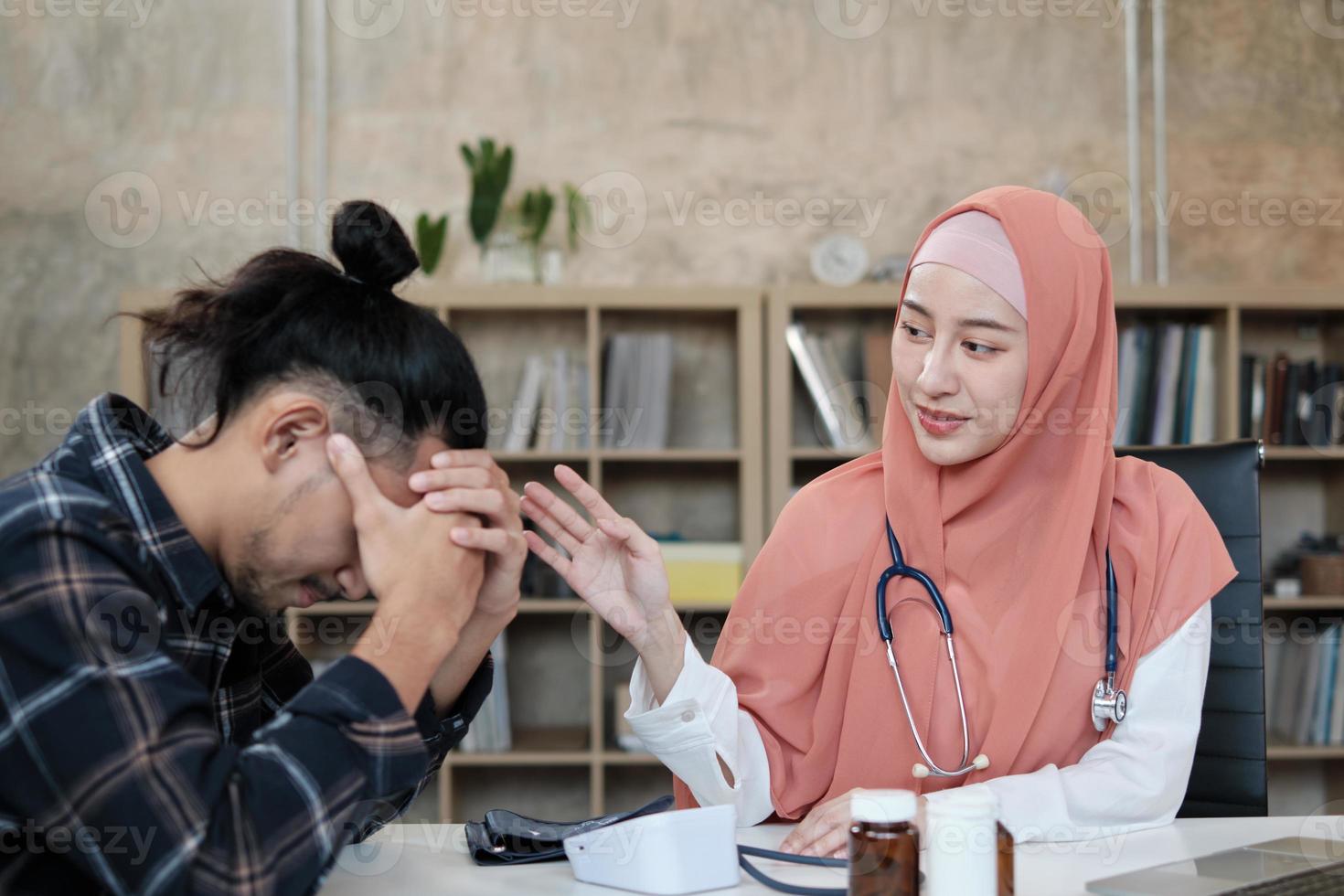 A young beautiful doctor, a person who is female Muslim encourages and comforting male patient of Asian ethnicity who is sad and illness, at health and medical treatment clinic's office in hospital. photo