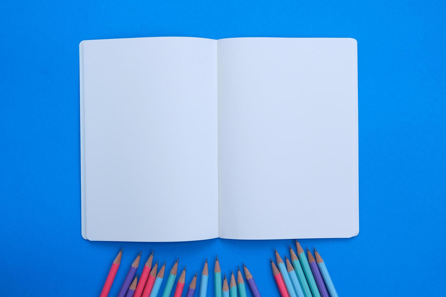 Blank notebook, a pencil, and space are on top of a blue office desk table. Flat lay, top view education concept photo