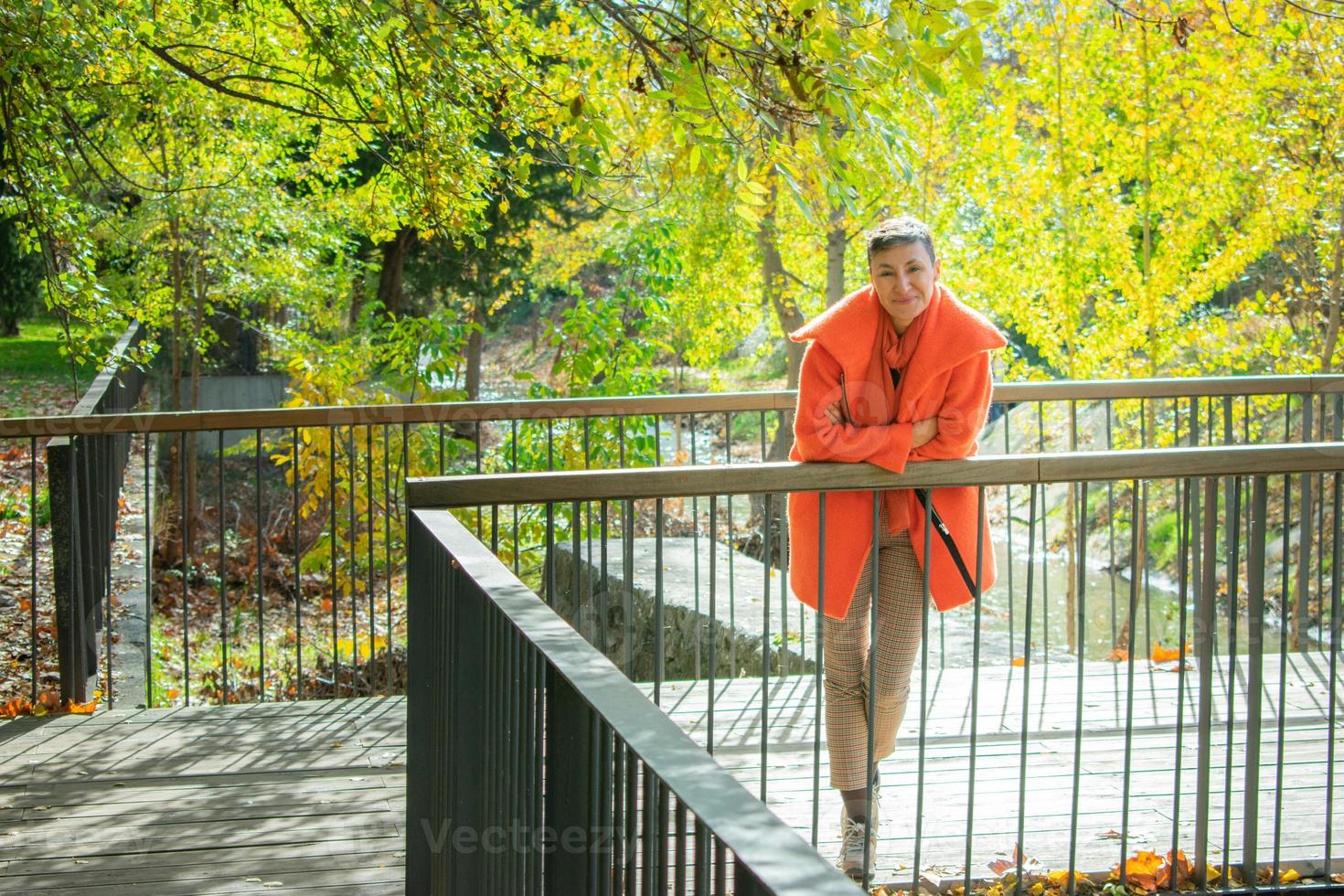 woman in orange coat leaning against metal railing photo
