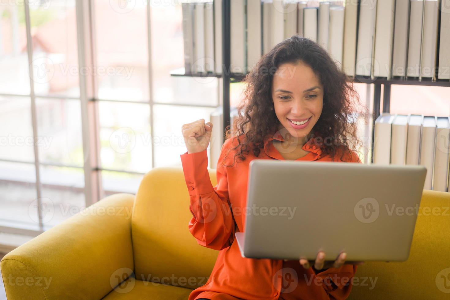 Mujer latina que trabaja con el portátil en el sofá con sentimiento feliz foto