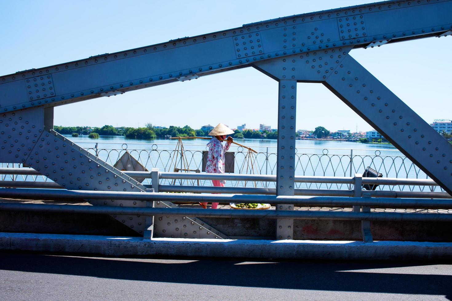persona irreconocible que va al mercado con un sombrero de paja cónico y un palo de transporte. cruzando el puente de hue. Vietnam foto