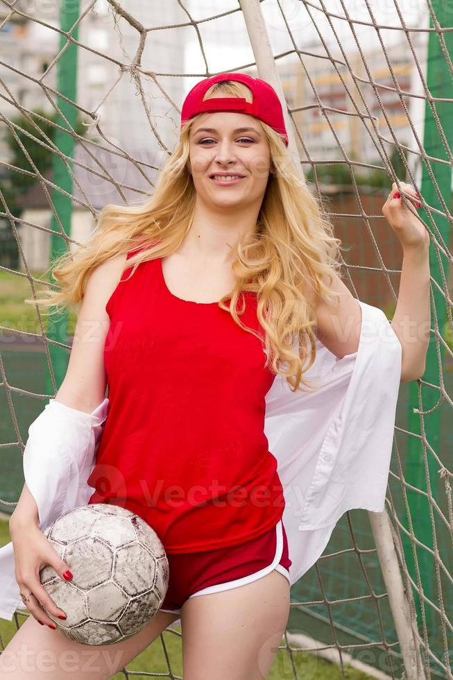 la rubia en forma roja con una pelota en la puerta del campo de fútbol. foto