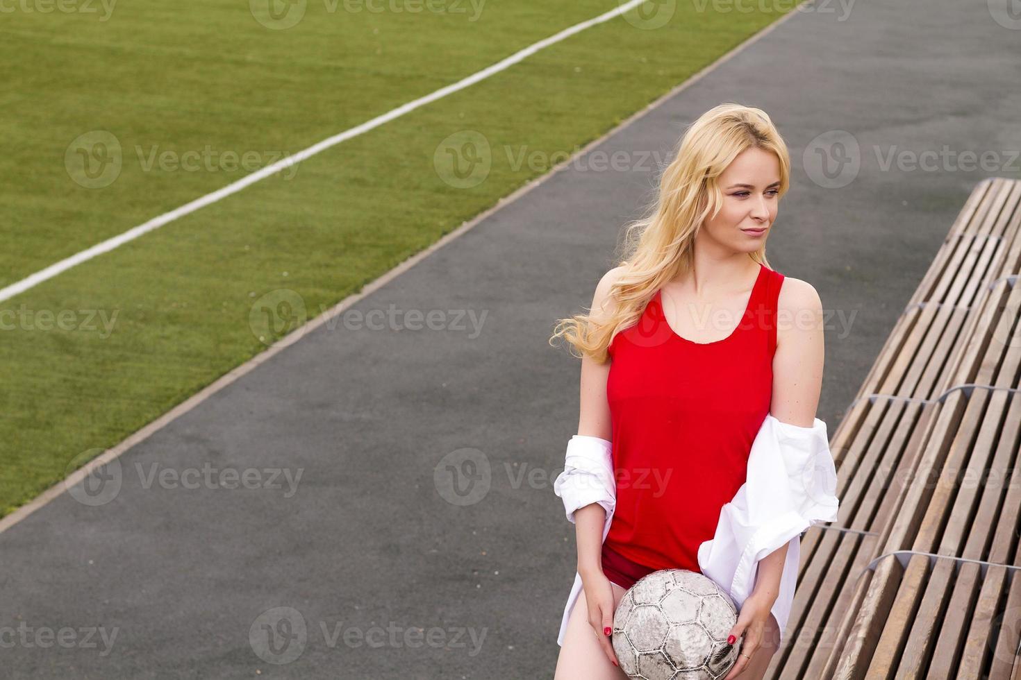 rubia con una pelota en el campo de fútbol con uniforme rojo. foto