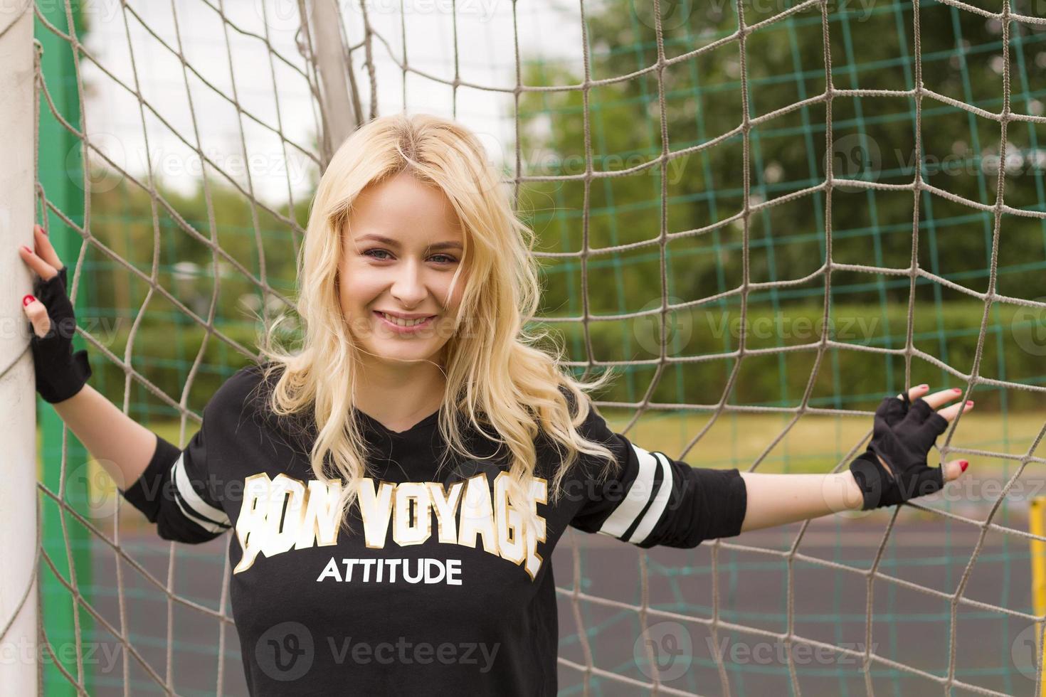 hermosa rubia dentro de la red de fútbol está sosteniendo y sonríe. foto