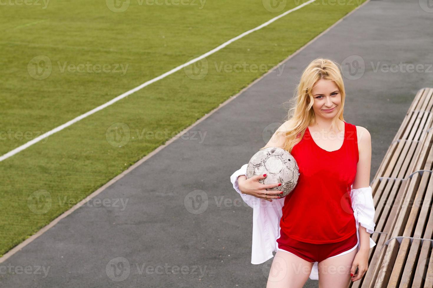 rubia con una pelota en el campo de fútbol con uniforme rojo. foto